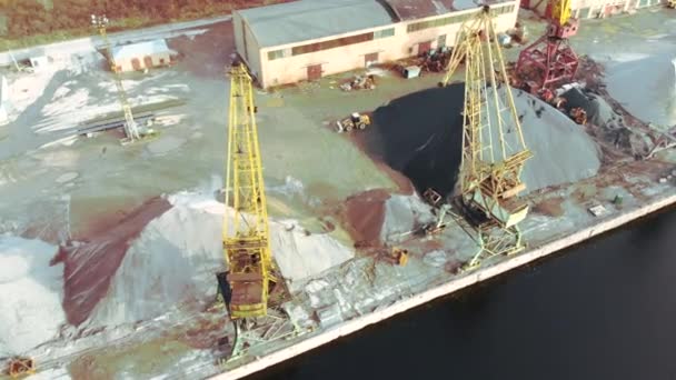 Hafenkräne am Flussufer produzieren Sand. Hafenkräne mit einem Eimer am Ufer des Flusses. Abbau von Flusssand. Hafenkräne extrahieren Flusssand, Produktion. Sonnenuntergang. Lastkahn. — Stockvideo