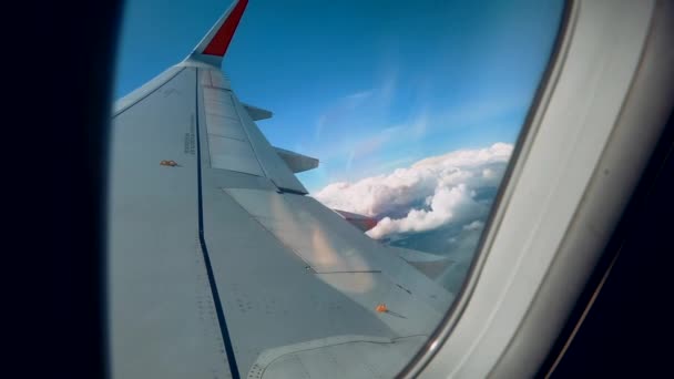 Hermosas nubes y un ala de avión por una ventana con un hermoso cielo azul. Disparo desde el ojo de buey de un avión mientras volaba a gran altitud con una hermosa vista de las nubes y el sol . — Vídeo de stock
