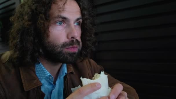 Homem barbudo comendo fast food close-up. Homem europeu com barba e cabelos longos comendo fast food close-up — Vídeo de Stock