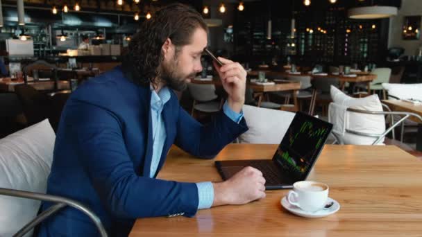 Fiatal európai üzletember álmos fáradt ül az asztalnál egy kávézóban egy csésze kávéval és egy laptoppal. Depressziós hangulat, fáradtság és állandó alváshiány, a városi élet nehézségei. — Stock videók