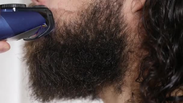 Przystojny młodzieniec z długimi włosami goli brodę przycinaczem w łazience. Zbliżenie. — Wideo stockowe