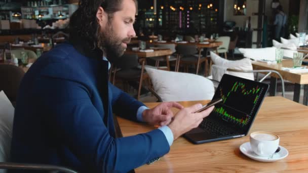 Νεαρός ευρωπαίος επιχειρηματίας κάθεται σε ένα τραπέζι σε ένα καφέ και πληκτρολογεί σε ένα φορητό υπολογιστή, ενώ εργάζεται σε ένα διάλειμμα για καφέ. — Αρχείο Βίντεο