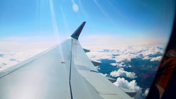 Nuvens bonitas e uma asa de avião fora de uma janela com um céu azul bonito. Tiro do pórtico de um avião enquanto voava em alta altitude com uma bela vista das nuvens e do sol . — Vídeo de Stock