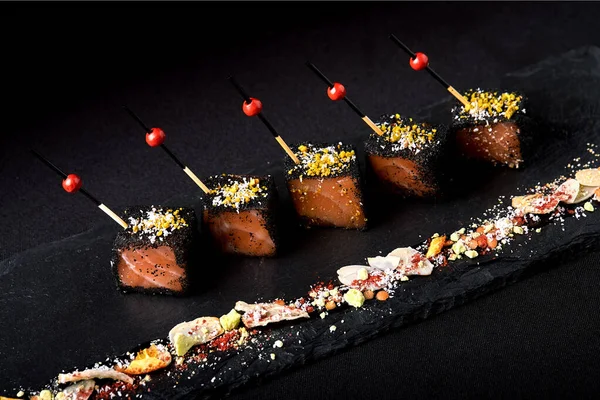 Ingelegde gesneden zalm in zwart brood, met spiesjes op een zwarte plaat. Fusion food concept, low key, kopieerruimte. — Stockfoto