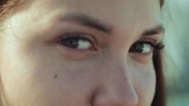 Das sommersprossige Gesicht einer dunkelhaarigen Frau mit schönen Augen blinzelt extrem langsam. attraktive junge Frau mit Wimpern, die in die Kamera schaut. — Stockvideo