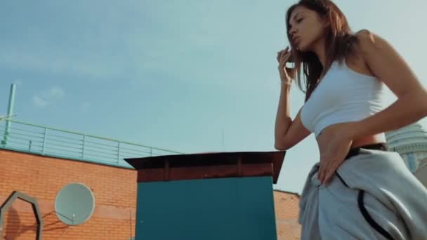 Handsome young woman feeling happy while listening music in the headphone, jumpping and dancing on a rooftop. — Stock Video