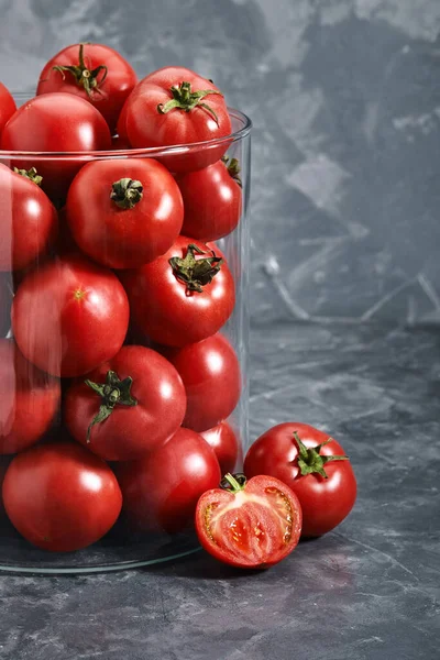 Tomates rojos medianos con un jarrón de vidrio sobre un fondo gris. Copiar espacio, abstracción, verduras frescas . —  Fotos de Stock