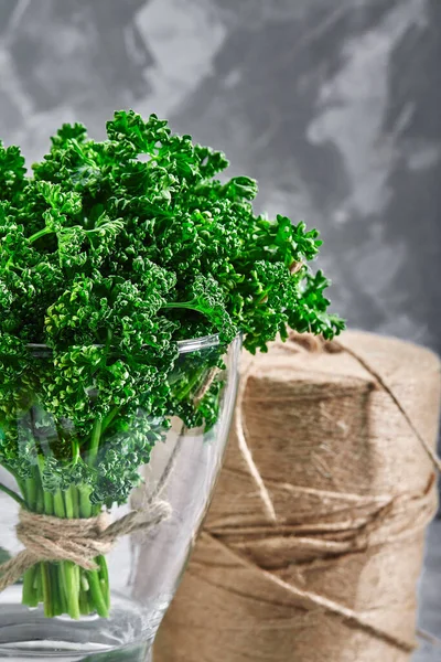 Un bouquet de persil frisé frais dans un vase avec de l'eau en gros plan sur un fond gris. Aliments frais, espace de copie . — Photo