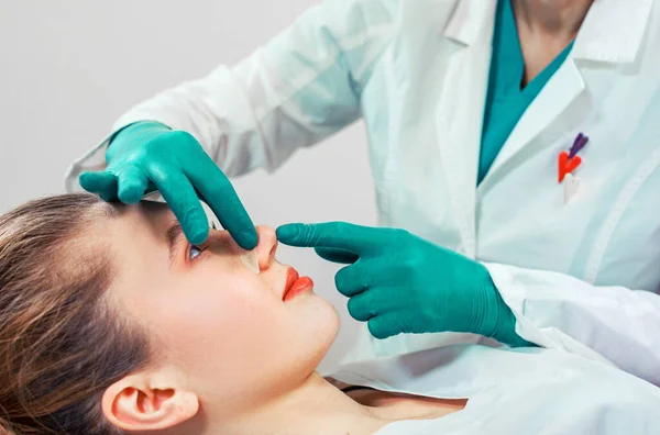 Rhinoplastika, chirurgické ruce se dotýkají nosu pacienta. Lidé, kosmetika, plastická chirurgie a kosmetika - chirurgické nebo kosmetologické ruce dotýkající se ženské tváře. — Stock fotografie