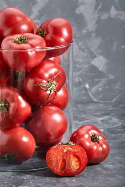 Fresh large tomatoes on a gray background. Whole and sliced tomatoes shot closeup with meta for text. Art concept tomatoes in the glass. — Stock Photo, Image