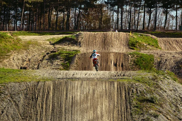 Motocross vezető akcióban gyorsítja a motorkerékpár felszáll, és ugrik ugródeszka a versenypályán. — Stock Fotó