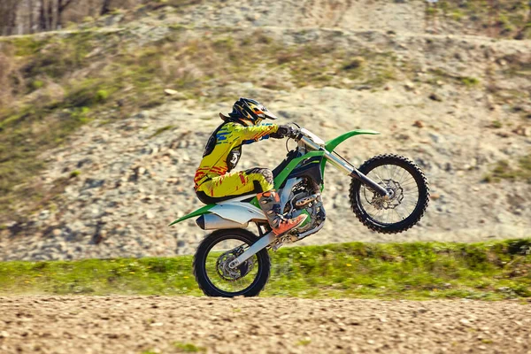 Piloto de motocross en acción acelerando el despegue de la moto y salta sobre un trampolín en la pista de carreras . — Foto de Stock