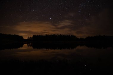 Night sky with starts in a  Conemara lake with Pine Forest aroun