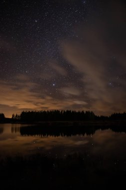 Night sky with starts in a  Conemara lake with Pine Forest aroun