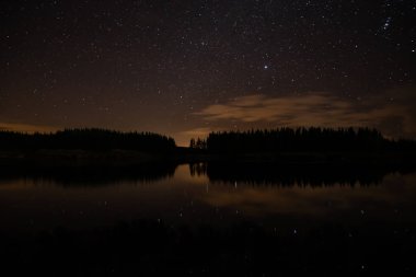Night sky with starts in a  Conemara lake with Pine Forest aroun
