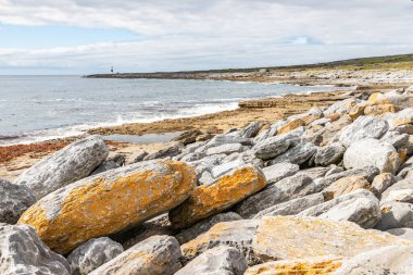Inisheer Adası 'nda arka planda deniz feneri olan kayalar ve plajlar.