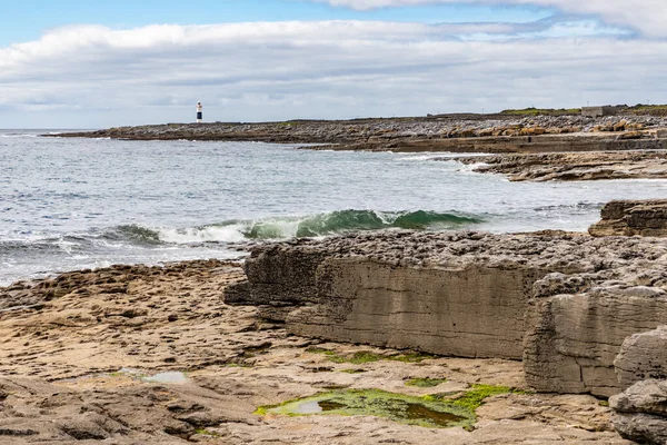 Skały i plaża z latarnią morską w tle na wyspie Inisheer — Zdjęcie stockowe