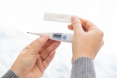 Termometre ve hamile testi tutan kadın el