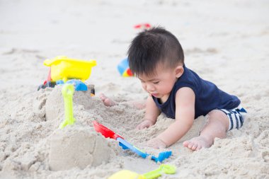 Tropik sahilde kum ile oynayan erkek bebek