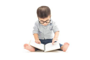 Beyaz arka plan üzerinde izole katta otururken şirin küçük çocuk oyun kitabı ve gözlük ile Asya bebek çocuk ve eğitim kavramı