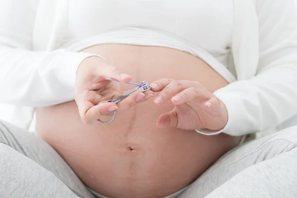 Mulher grávida cortando unhas mão por cortador de unhas em branco bedfather brincando com o filho bonito e segurando em seus braços em casa, conceito de pai e menino — Fotografia de Stock