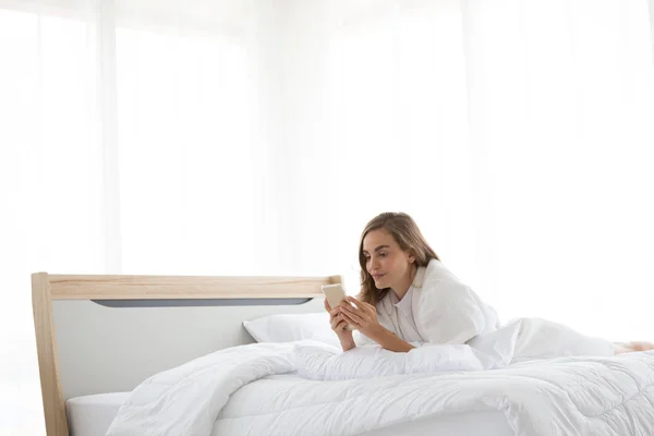 Zrelaksowany kaukaski kobieta za pomocą smartfona rano na łóżku w sypialni w domu — Zdjęcie stockowe