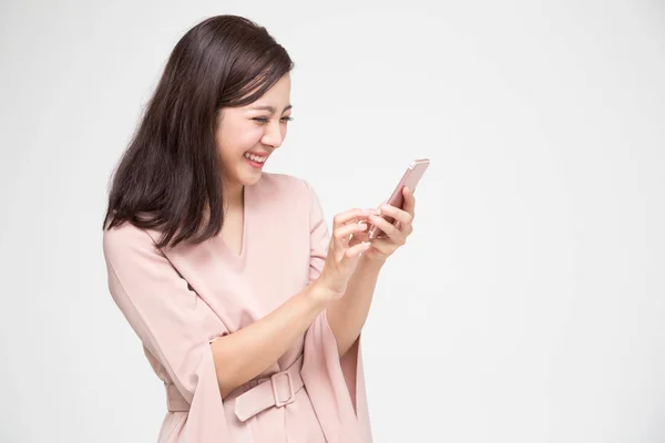 Веселая молодая азиатка, пользующаяся смартфоном и получающая хорошие новости из сообщения в мобильном чате на белом фоне — стоковое фото