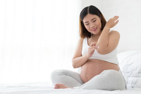 Pregnant woman takes care of elbow using cosmetic cream, Asian model — Stock Photo, Image