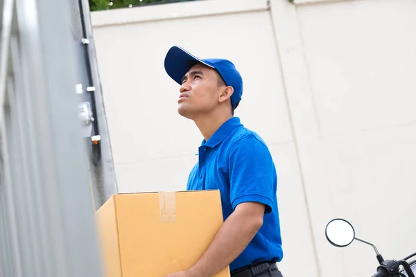 Entrega hombre sosteniendo la caja de paquete de pie en frente de la casa —  Fotos de Stock