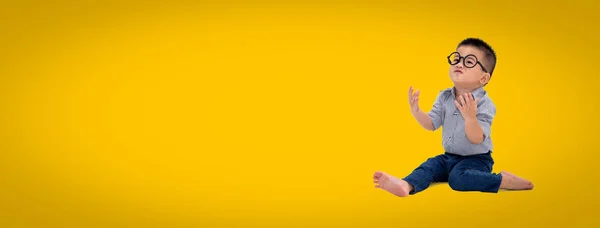 Asian little boy wearing eyeglasses and sitting on floor isolate on yellow background — Stock Photo, Image