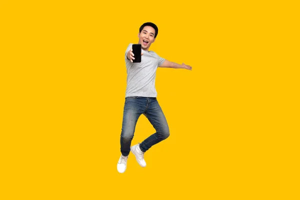 Asian man jumping and presenting mobile phone isolated on yellow background — Stock Photo, Image