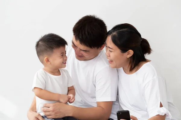 Щаслива молода Азіатська сім'я з трьох посміхаючись і відпочиваючи в білих футболках на білому фоні — стокове фото