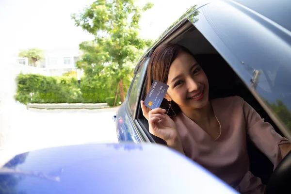 Glad ung asiatisk kvinna håller betalkort eller kreditkort och används för att betala för bensin, diesel och andra bränslen vid bensinstationer, Driver med flottan kort för att tanka bilen — Stockfoto