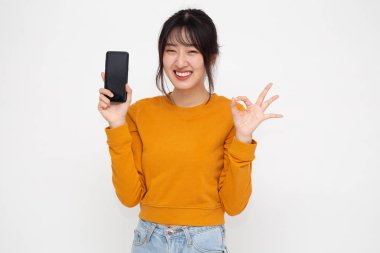 Portrait of beautiful Asian teenager wowan showing or presenting mobile phone application on hand and ok sign isolated over white background clipart