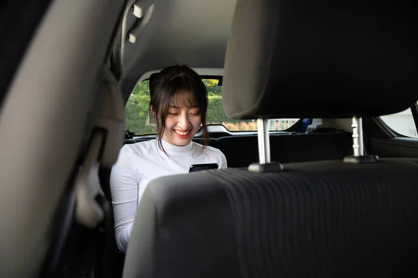 Asiática adolescente mujer usando un teléfono inteligente en el asiento trasero del coche, Los pasajeros utilizan una aplicación para pedir un paseo y Peer-to-peer paseo concepto de compartir —  Fotos de Stock