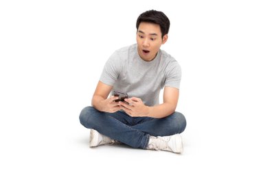Genç Asyalı adam wow ifade ve beyaz arka plan üzerinde izole akıllı telefon kullanırken katta oturan