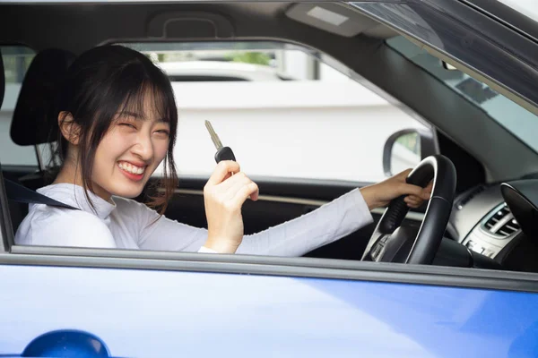Молодая счастливая азиатская женщина-водитель улыбается и показывает ключи от новой машины. Концепция начинающих пилотов — стоковое фото