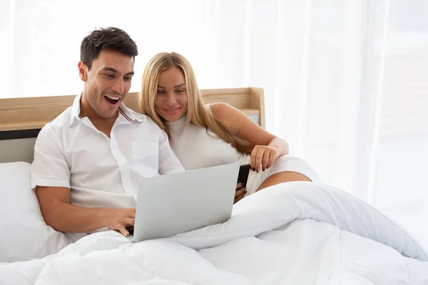 Kaukasisches Paar sucht billiges Flugticket und Hotel im Internet online mit Laptop im Bett, bereitet und findet erstaunliche Unterkünfte für Urlaubskonzept — Stockfoto
