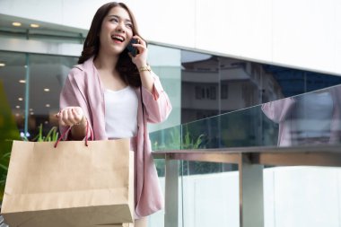 Asyalı güzel kız telefonda arkadaşıyla konuşuyor ve elinde alışveriş çantası var.