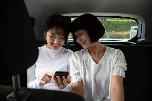 Mujer adolescente asiática y mujer mayor utilizando un teléfono inteligente en el asiento trasero del coche, Los pasajeros utilizan una aplicación para pedir un paseo y Peer-to-peer concepto de compartir paseo —  Fotos de Stock