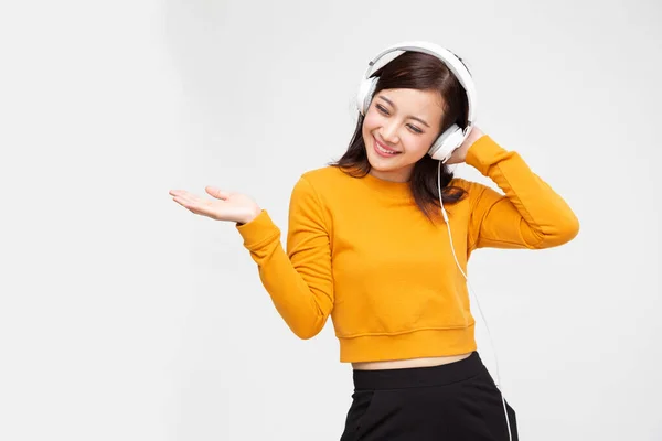 年轻的亚洲美女一边听音乐一边用耳机听音乐，一边用独立于白人背景的智能手机播放音乐，带着富有灵感的面部表情概念跳舞 — 图库照片