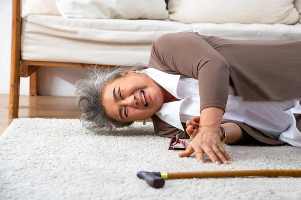 Asian senior woman falling down on carpet and lying on the floor in living room at home, Falls of older adults concept