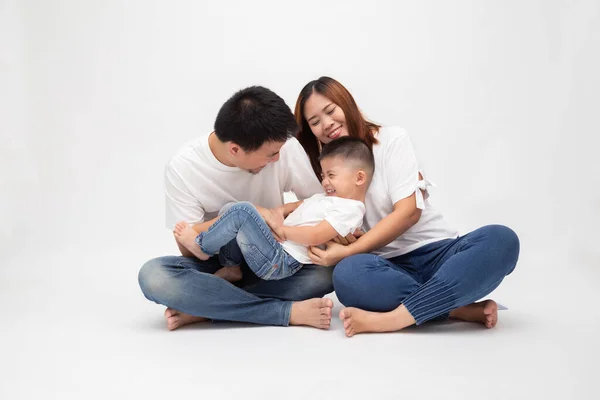 Cheerful Asian family sitting over white background have fun father tickling little son. Young couple with kids wearing white top and blue jeans. Parents enjoy free time playing concept