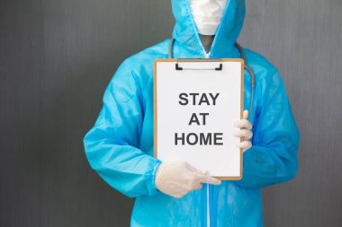 Beyaz maskeli ve beyaz kağıtlı PPE giysisi giyen doktor evde kalıp Coronavirus veya Covid-19 salgınından korur.