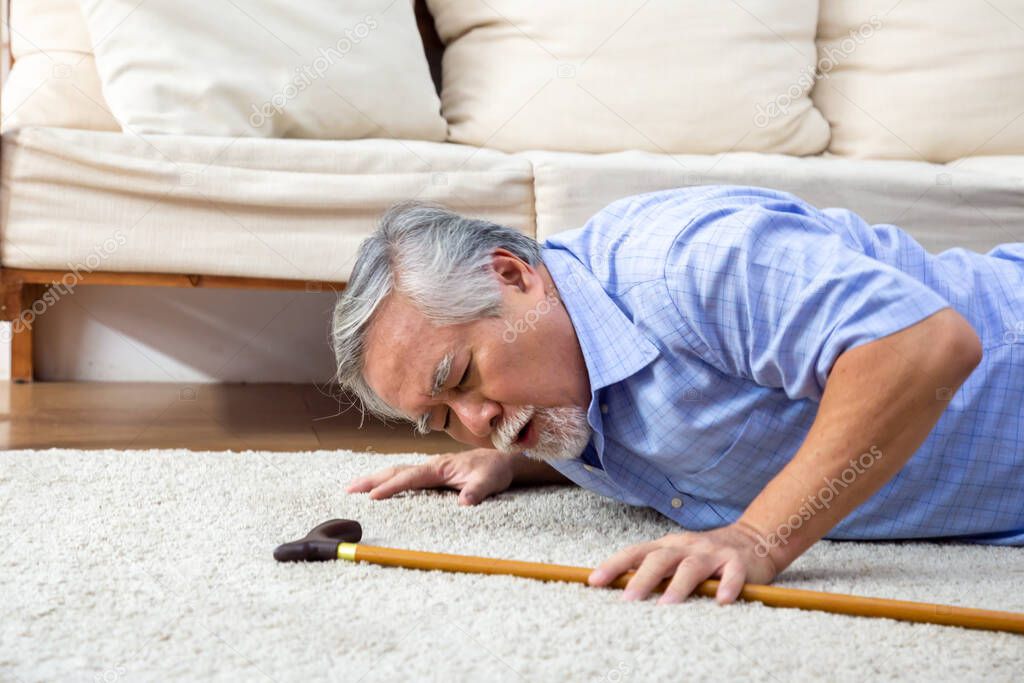 Asian senior man falling down on carpet and lying on the floor in living room at home, Falls of older adults concept