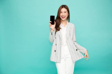 Mutlu Asyalı kadın gülümsüyor ve cep telefonunu açık yeşil arka planda yalnız tutuyor.