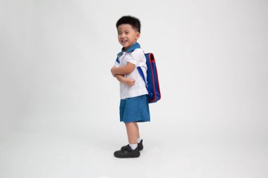 Sırt çantalı neşeli Asyalı küçük çocuk beyaz arka planda izole edilmiş eğleniyor..