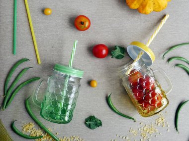 Domates ve kuşkonmaz fasulye, taze su bardağı ve gri açık renkli, üstten görünüm üzerine kokteyl boruları, dekoratif mevsimlik bileşimi