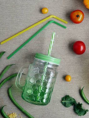 Domates ve kuşkonmaz fasulye, taze su bardağı ve gri açık renkli, üstten görünüm üzerine kokteyl boruları, dekoratif mevsimlik bileşimi