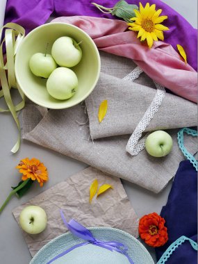 Elma, sarı yaprakları, yeşil şapka ve hafif bir arka plan gri tuval ve pembe ve mor bez, taze çiçekler görünümü top. Mevsimlik dekoratif kompozisyon, natürmort. Yaz, sonbahar